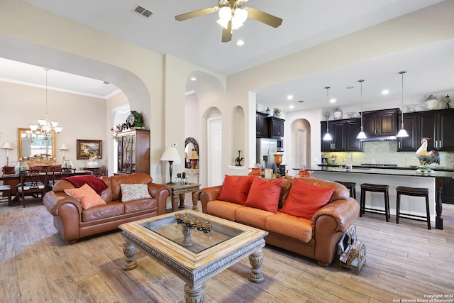 living room with ceiling fan with notable chandelier, ornamental molding, and light hardwood / wood-style floors