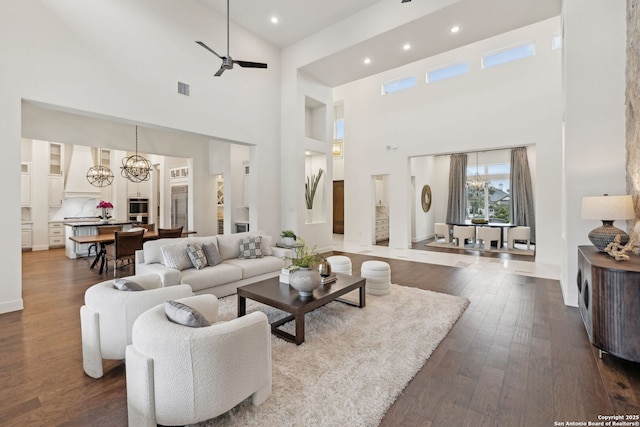 living room with a towering ceiling, wood-type flooring, and ceiling fan with notable chandelier