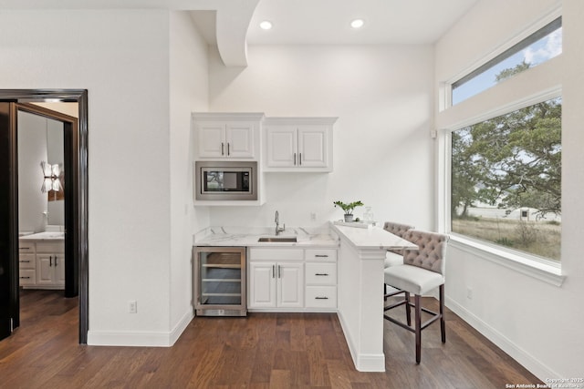 bar with beverage cooler, dark wood-type flooring, stainless steel microwave, white cabinets, and sink