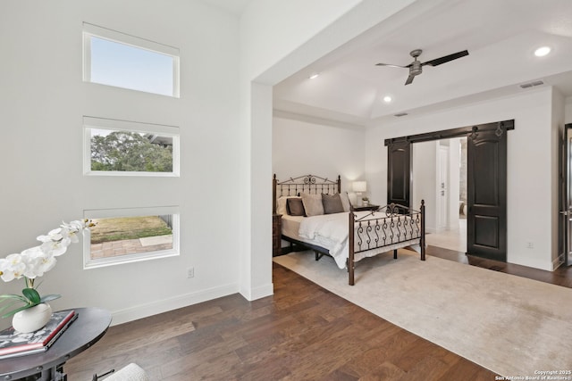 bedroom featuring a towering ceiling, ceiling fan, a barn door, and dark wood-type flooring