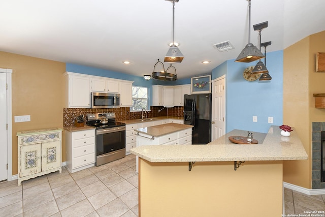 kitchen featuring appliances with stainless steel finishes, decorative light fixtures, white cabinetry, a kitchen bar, and kitchen peninsula