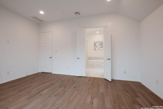 unfurnished bedroom featuring vaulted ceiling, ensuite bathroom, and hardwood / wood-style floors