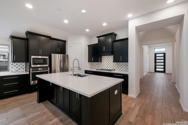 kitchen with sink, backsplash, an island with sink, and appliances with stainless steel finishes