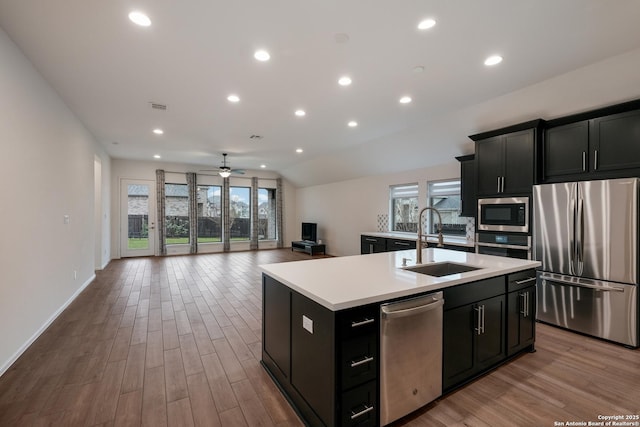 kitchen with appliances with stainless steel finishes, sink, a kitchen island with sink, ceiling fan, and light hardwood / wood-style flooring