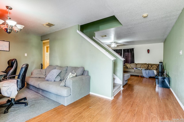 living room featuring ceiling fan with notable chandelier, light wood-type flooring, and a textured ceiling