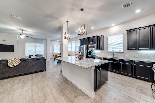 kitchen with stainless steel appliances, decorative light fixtures, a center island, light hardwood / wood-style flooring, and light stone countertops