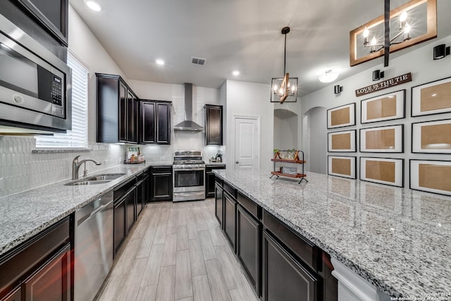 kitchen featuring stainless steel appliances, sink, decorative light fixtures, light stone countertops, and wall chimney range hood