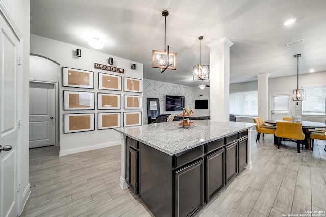 kitchen with decorative light fixtures, light stone counters, a kitchen island, and ornate columns