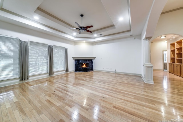 unfurnished living room with a raised ceiling, decorative columns, light wood-type flooring, a fireplace, and ceiling fan