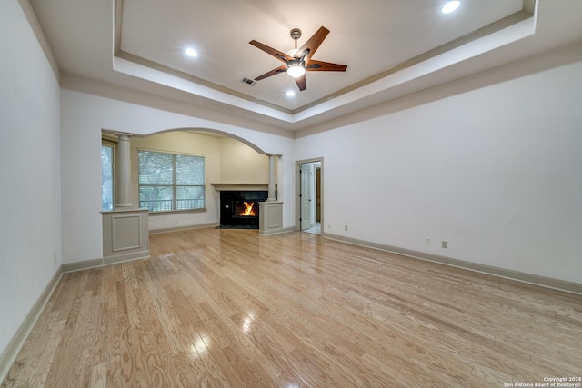 unfurnished living room featuring decorative columns, a raised ceiling, ceiling fan, light hardwood / wood-style flooring, and a high end fireplace