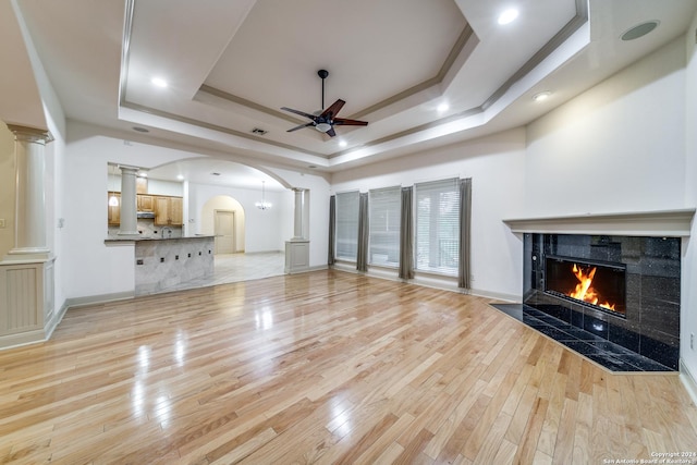 unfurnished living room featuring a tile fireplace, ceiling fan, a tray ceiling, and light hardwood / wood-style flooring