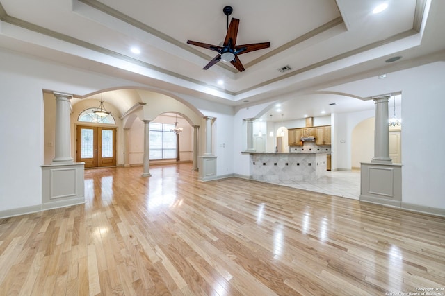 unfurnished living room featuring french doors, light wood-type flooring, ceiling fan, a tray ceiling, and ornamental molding