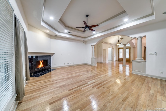 unfurnished living room with ornate columns, a raised ceiling, ceiling fan, light hardwood / wood-style floors, and a premium fireplace