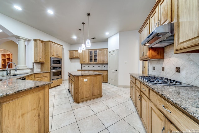 kitchen featuring ornate columns, stainless steel appliances, stone counters, a kitchen island, and sink