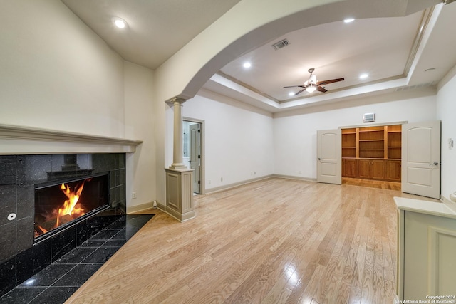 unfurnished living room with light hardwood / wood-style floors, a raised ceiling, ceiling fan, and a tile fireplace