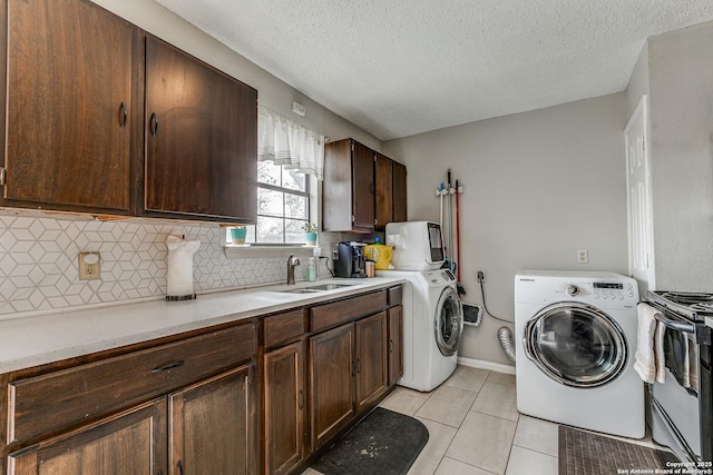 clothes washing area with a textured ceiling, washing machine and dryer, light tile patterned floors, cabinets, and sink