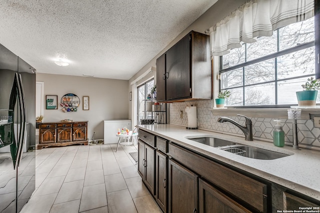 kitchen featuring sink, a textured ceiling, backsplash, and black fridge