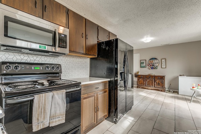 kitchen with black appliances, light tile patterned flooring, a textured ceiling, and tasteful backsplash