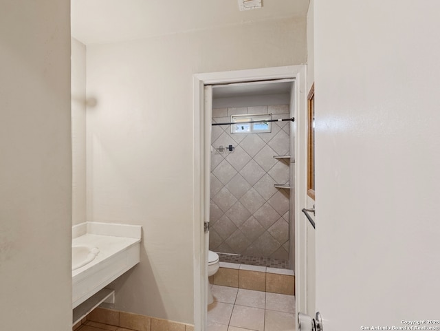 bathroom featuring toilet, tiled shower, and tile patterned floors