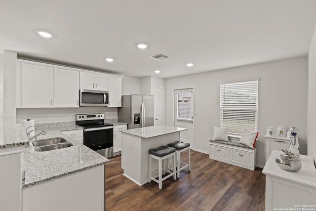 kitchen with white cabinets, a kitchen island, stainless steel appliances, dark hardwood / wood-style floors, and light stone counters