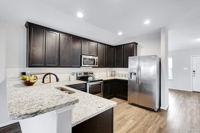 kitchen featuring light stone counters, kitchen peninsula, sink, stainless steel appliances, and dark brown cabinetry