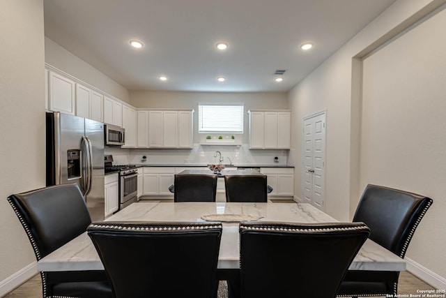 kitchen featuring stainless steel appliances, light stone countertops, white cabinets, and a center island