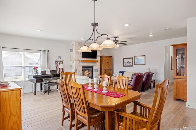 dining room with light wood-type flooring, ceiling fan, and a stone fireplace