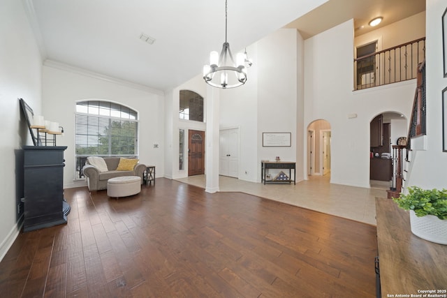 living area featuring crown molding, an inviting chandelier, a towering ceiling, and hardwood / wood-style flooring