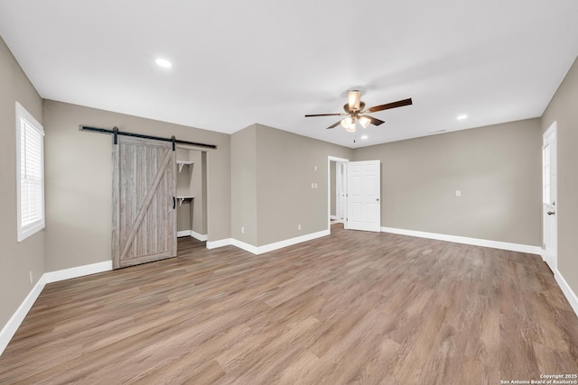 spare room featuring light wood-type flooring, ceiling fan, and a barn door