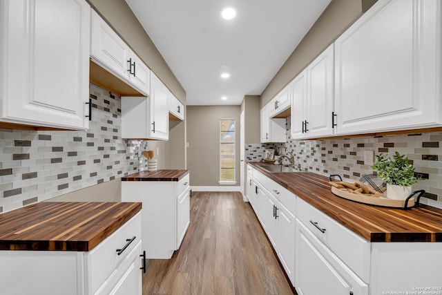 kitchen with light wood-type flooring, wood counters, decorative backsplash, sink, and white cabinetry