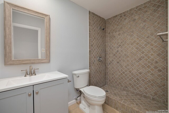 bathroom with toilet, a tile shower, vanity, and tile patterned floors