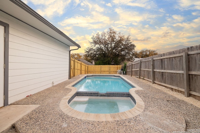 pool at dusk featuring an in ground hot tub