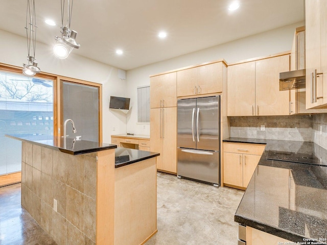 kitchen featuring decorative light fixtures, light brown cabinets, a center island with sink, and stainless steel refrigerator