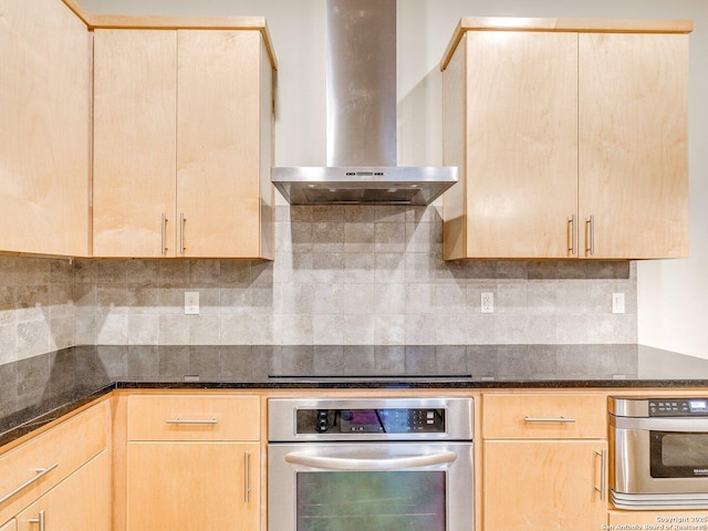 kitchen with dark stone countertops, stainless steel oven, light brown cabinetry, and wall chimney exhaust hood