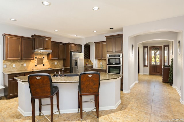 kitchen featuring stainless steel appliances, light stone countertops, a kitchen island with sink, and sink