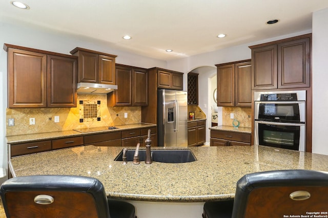 kitchen with light stone counters, appliances with stainless steel finishes, sink, and a breakfast bar area