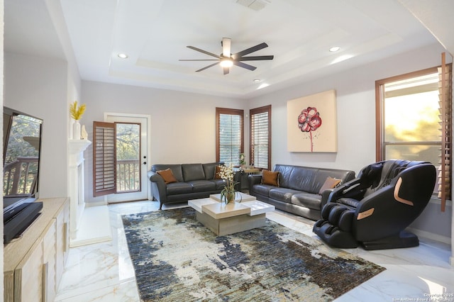 living room with a wealth of natural light, ceiling fan, and a tray ceiling