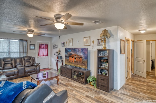 living room featuring light wood-type flooring, ceiling fan, and a textured ceiling