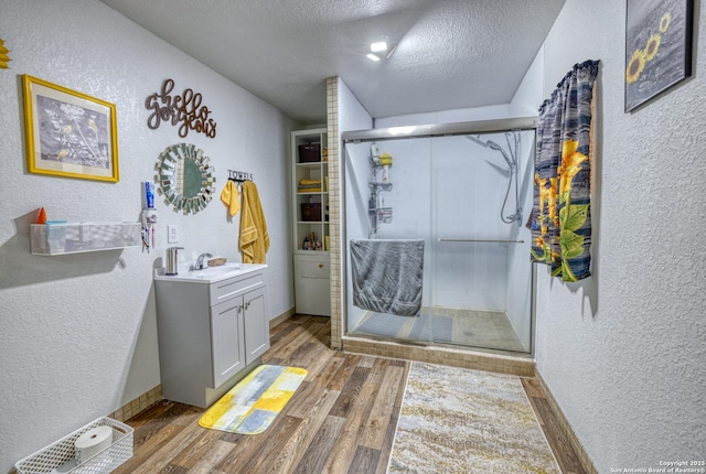 bathroom featuring a textured ceiling, a shower with door, wood-type flooring, and vanity