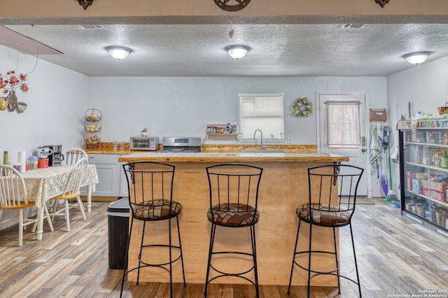 kitchen with stainless steel electric stove, light hardwood / wood-style floors, a kitchen bar, white cabinets, and sink