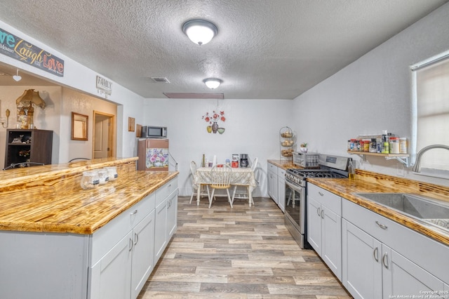 kitchen with a textured ceiling, stainless steel appliances, light wood-type flooring, white cabinetry, and sink