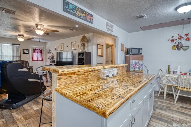 kitchen featuring white cabinets, a textured ceiling, ceiling fan, and hardwood / wood-style flooring