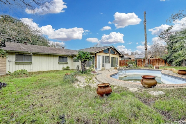 rear view of house with a fenced in pool and a lawn