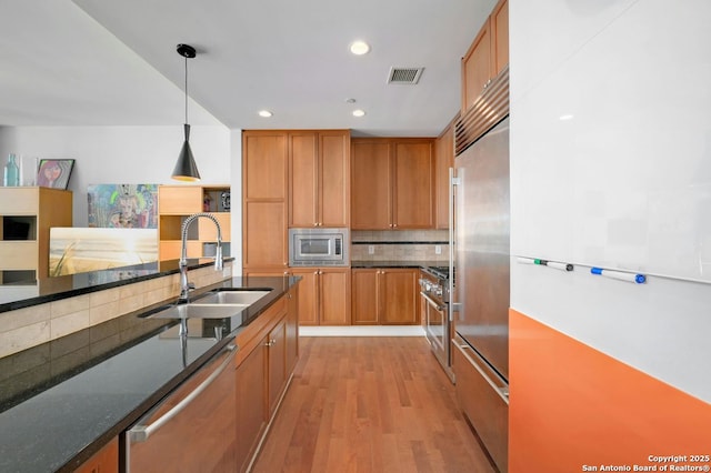 kitchen featuring appliances with stainless steel finishes, tasteful backsplash, decorative light fixtures, light hardwood / wood-style flooring, and sink