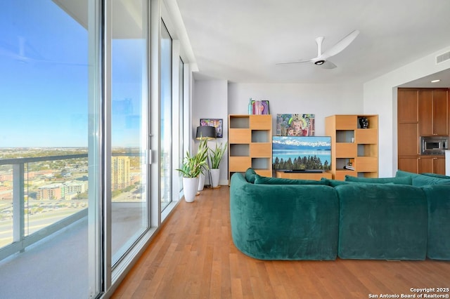 living room with light wood-type flooring, ceiling fan, a healthy amount of sunlight, and a wall of windows