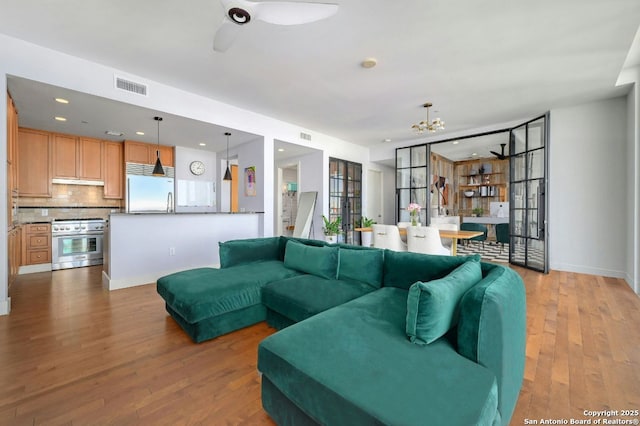 living room featuring ceiling fan with notable chandelier and light hardwood / wood-style flooring