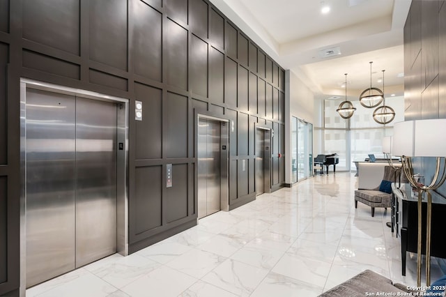 hall with an inviting chandelier, a raised ceiling, and elevator