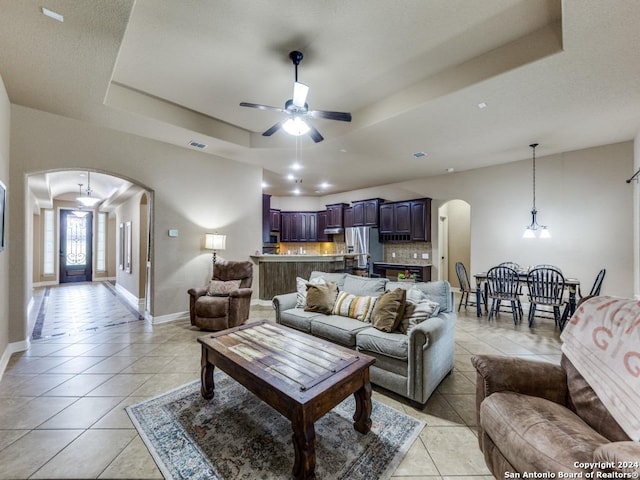 living room featuring ceiling fan with notable chandelier, a tray ceiling, and light tile patterned flooring