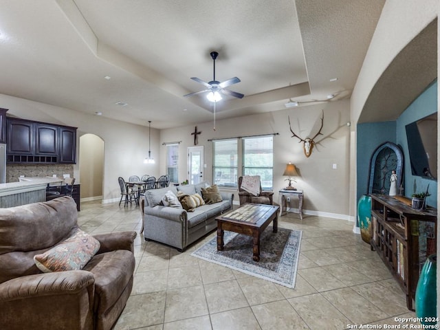 living room featuring ceiling fan, a raised ceiling, and light tile patterned flooring