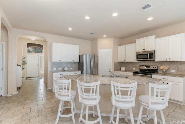 kitchen featuring appliances with stainless steel finishes, white cabinets, a center island with sink, and sink